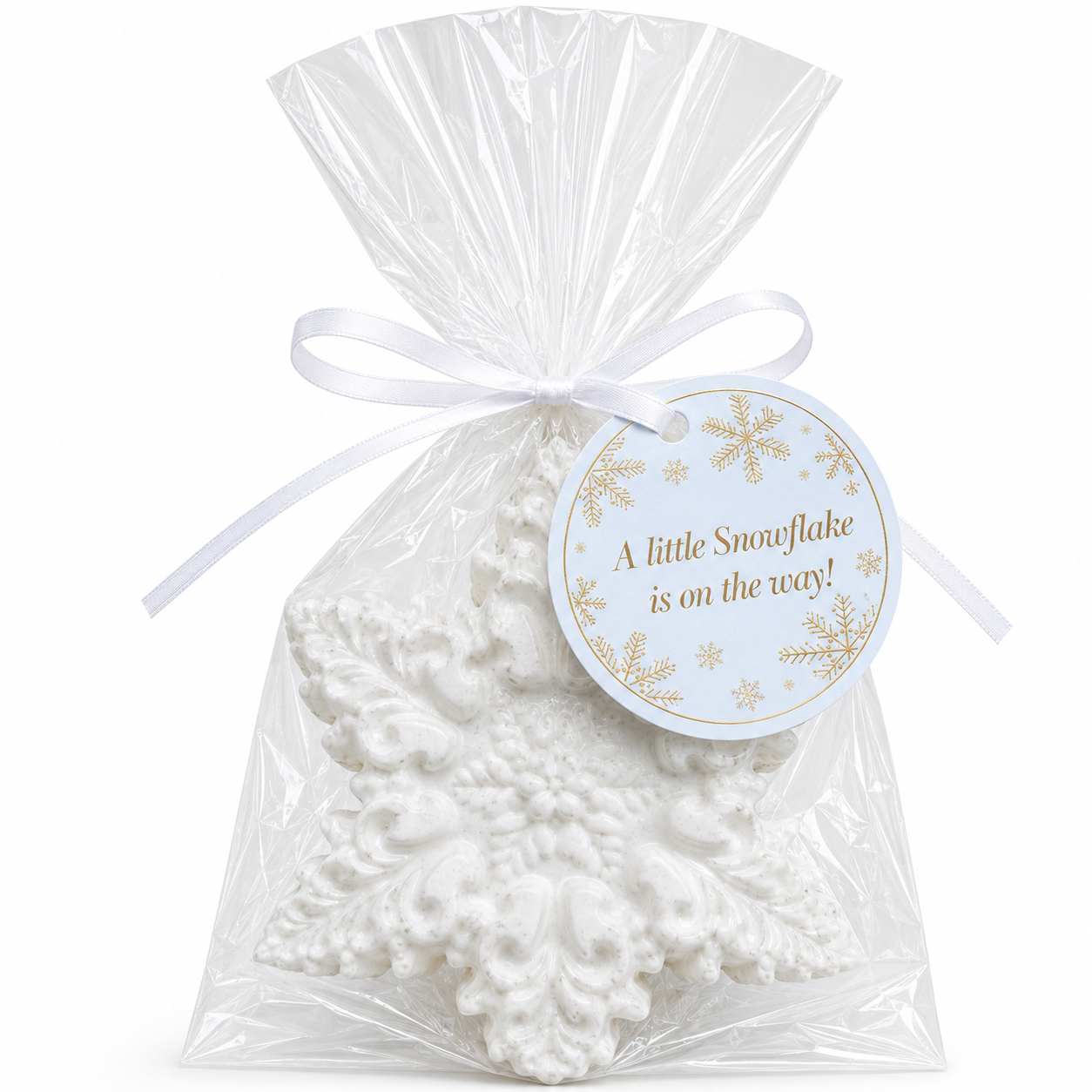 A white snowflake-shaped item wrapped in clear cellophane and tied with a white ribbon, with a round tag that reads 'A little Snowflake is on the way!'.